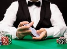 dealer sitting at a poker table with cards and chips in front of him