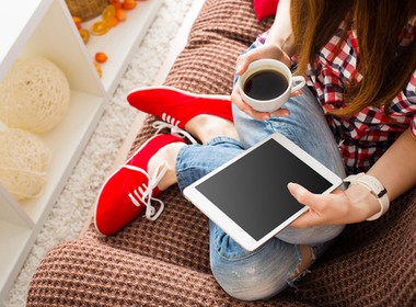 woman relaxing on her sofa with her tablet and a cup of coffee