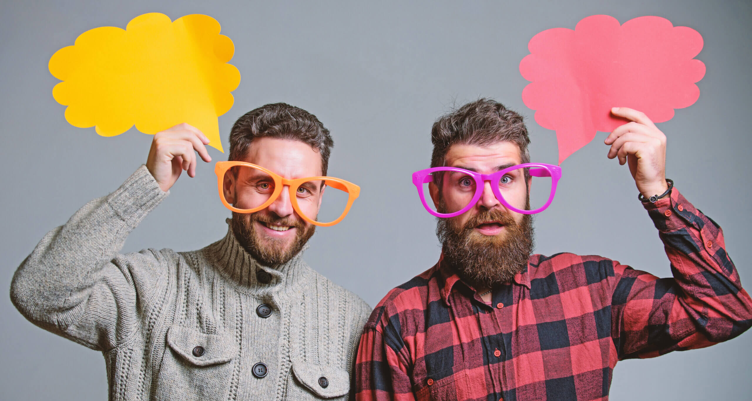 two smiling bearded men in their twenties wearing very over-sized glasses for fun.