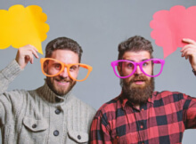 two smiling bearded men in their twenties wearing very over-sized glasses for fun.