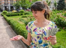 woman in a pretty print dress in a green outdoor setting smiling she looks at a casino chip that fell into her hand