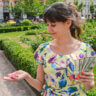 woman in a pretty print dress in a green outdoor setting smiling she looks at a casino chip that fell into her hand