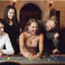 two women and three men smiling broadly as they play a table game at a casino. The key element here is that they are smiling.