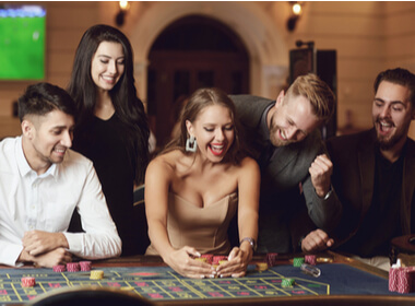 two women and three men smiling broadly as they play a table game at a casino. The key element here is that they are smiling.