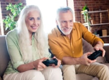 older white haired couple smiling as they playa casual game on the sofa