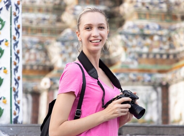 smiling young woman in a pink top enjoying her vacation by taking pictures with a camera