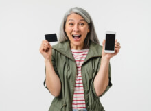Grey-haired woman very happily showing her mobile phone and credit card. She has just signed up at an online casino.