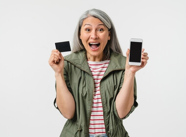 Grey-haired woman very happily showing her mobile phone and credit card. She has just signed up at an online casino.