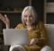 Smiling Fortyish woman with long straight white hair comfortably on a sofa and playing online casino games on her laptop