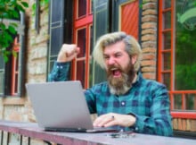 bearded and white haired man playing online video poker and celebrating a big win.