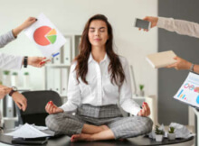 a young businesswoman meditating as colleagues urge her to pay attention to business matters