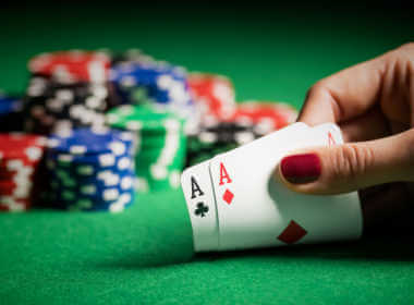 a woman's hand with bright red nail polish showing pocket aces at the poker table