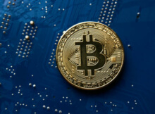 a light gold bitcoin with a black B against a blue microchip circuit to show that bitcoins are digital currency