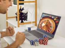 young man happily playing a casino game on his laptop with "chips" at the side of the computer