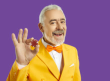 smiling older man with moustache, yellow sports jacket, orange bow tie holding a casino chip