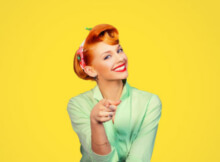 a pretty red-head woman with a 1950's look in her hairdo, her make-up, and her dress.