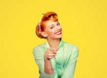 a pretty red-head woman with a 1950's look in her hairdo, her make-up, and her dress.