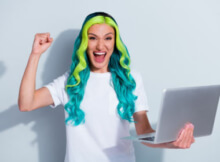 young woman with long hair in neon green and light green excitedly playing on her laptop at an online casino