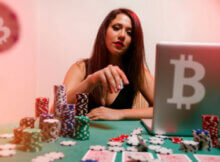 attractive woman playing at an online casino with the bitcoin sign on her laptop and many stacks of casino chips on the table