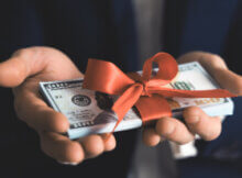 a stack of hundred dollar bills tied by a ribbon and held by a man's hands to symbolize receiving a bonus.