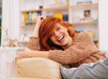 attractive red headed woman on her sofa laughing her head off showing the existential value of a good sense of humor