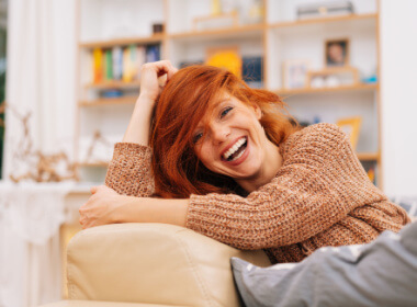 attractive red headed woman on her sofa laughing her head off showing the existential value of a good sense of humor