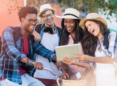 inter-racial group of two young men and two young women enjoying a game on a tablet