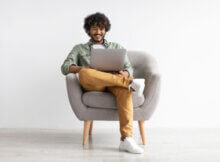 happy young man sitting comfortably on a living room chair with his laptop