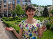 European woman smiling showing winnings from playing online casino games. In the background are old beautiful European buildings