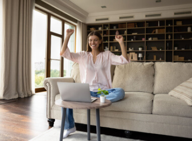 happy young woman sitting comfortably on her sofa cheering as she wins playing at an online casino