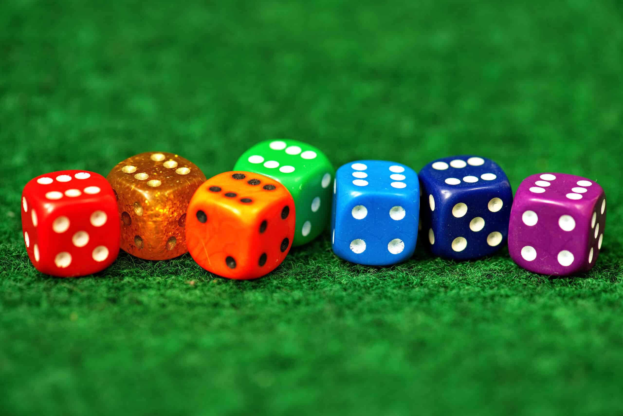 seven dice all of a different color laid out on a green felt table all showing the number six