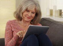 a happy grey and proud woman accessing social media sites on a tablet while comfortably seated on her sofa