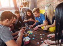 seven young adult friends all smiling as they play a group board game together