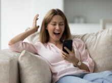 a young woman relaxing on her sofa smiling broadly possibly getting a big bonus from an online casino