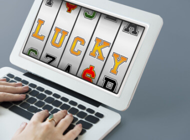 a woman's fingers on a keyboard as she plays a progressive slot with the word LUCKY on the slots