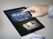 a touch screen tablet with online poker on the screen. there are three aces and a man is touching the screen.