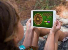 young woman on hiking trail taking a break and playing online roulette on her tablet