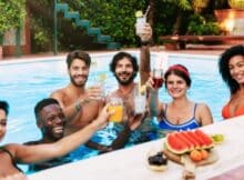 six young adults, three women and three men, enjoying the pool with drinks at a hotel resort