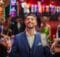 A man enjoying himself immensely at a land-based casino. He has a blue suit and vest with a short beard and mustache and no tie.